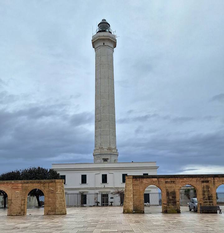 A tall coastal lighthouse and attached building stand beneath a gray sky.