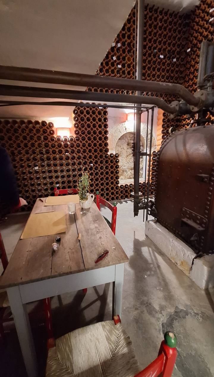 An atmospheric wine cellar lined with hundreds of dusty bottles and rustic tables.
