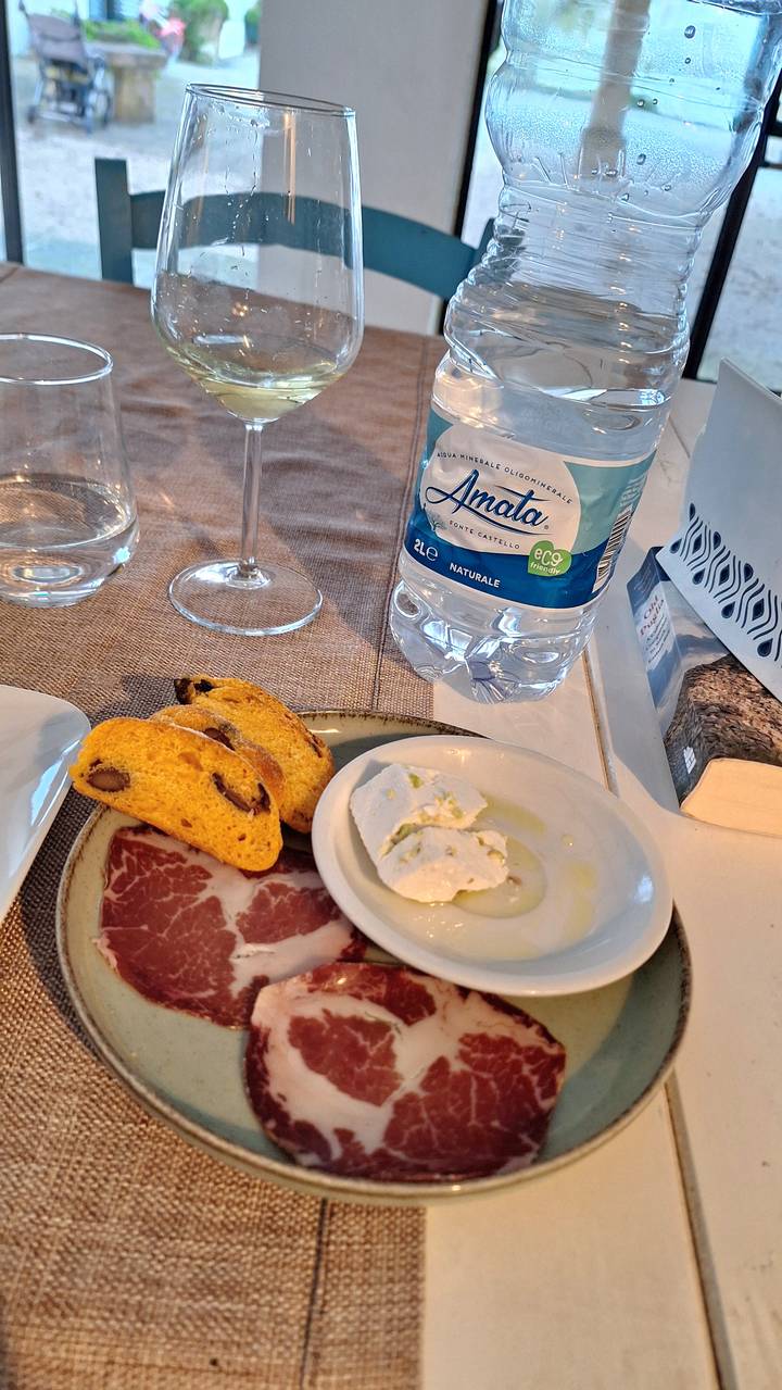 A snack plate with biscotti, cured meat and fresh cheese beside bottled water.
