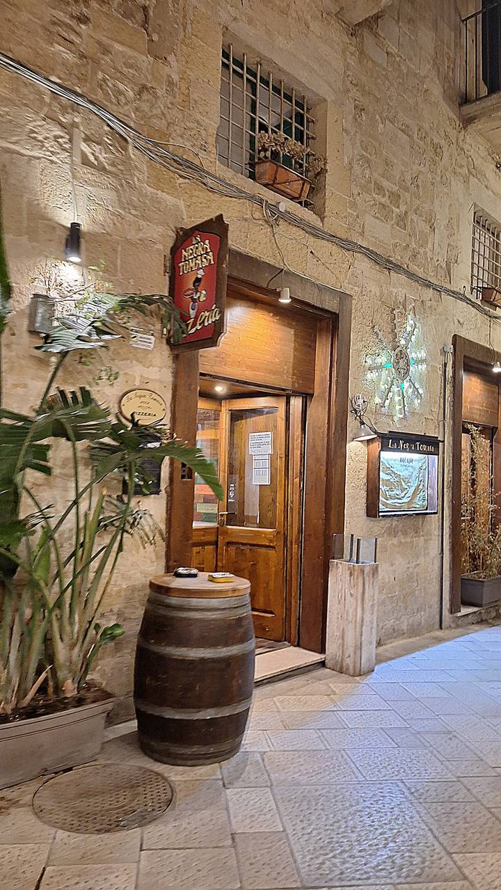 Stone-walled pizzeria entrance with wooden door, signage and warm evening lighting.