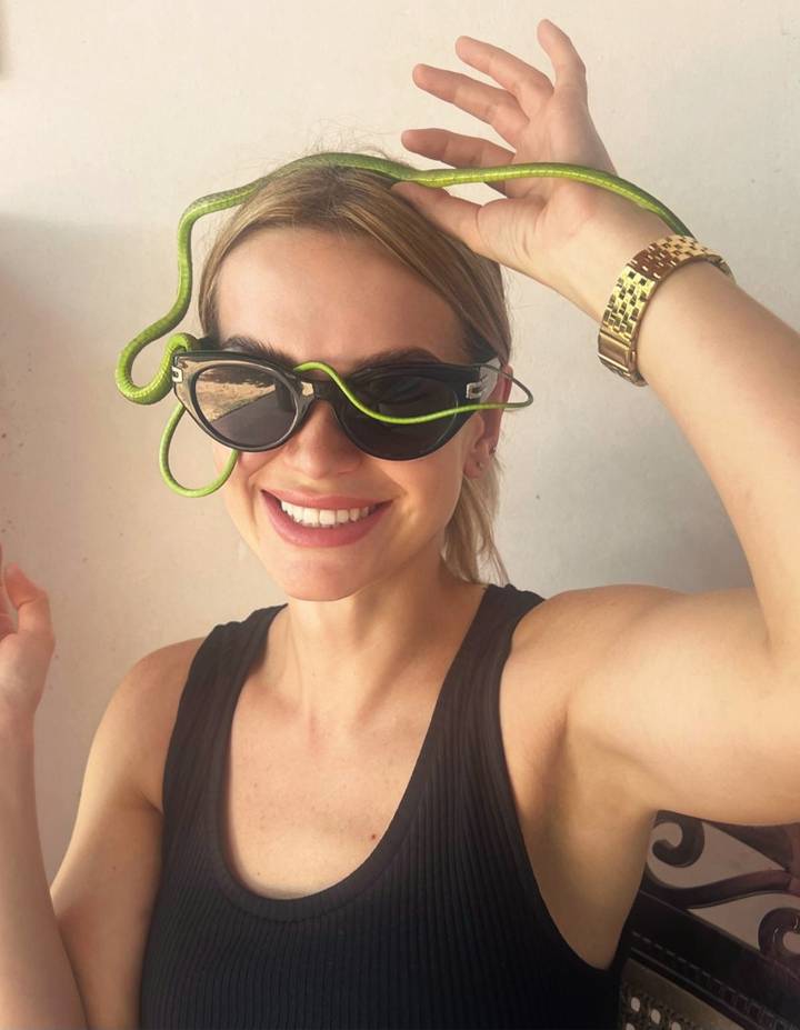 Smiling woman wearing sunglasses playfully drapes a small green snake over the frames