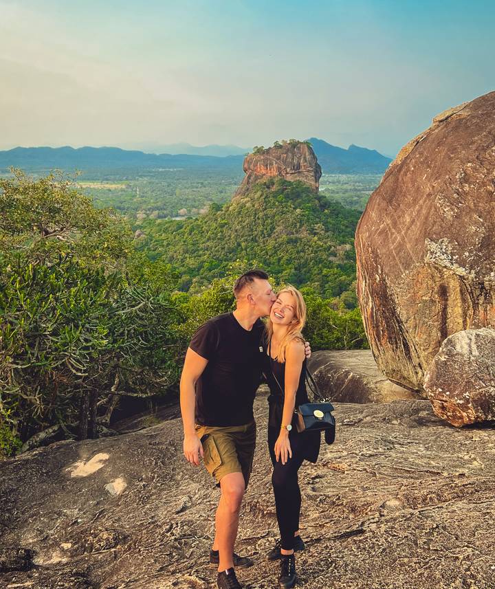 Couple sharing a kiss on a rocky ledge with the dramatic Sigiriya Rock rising behind them