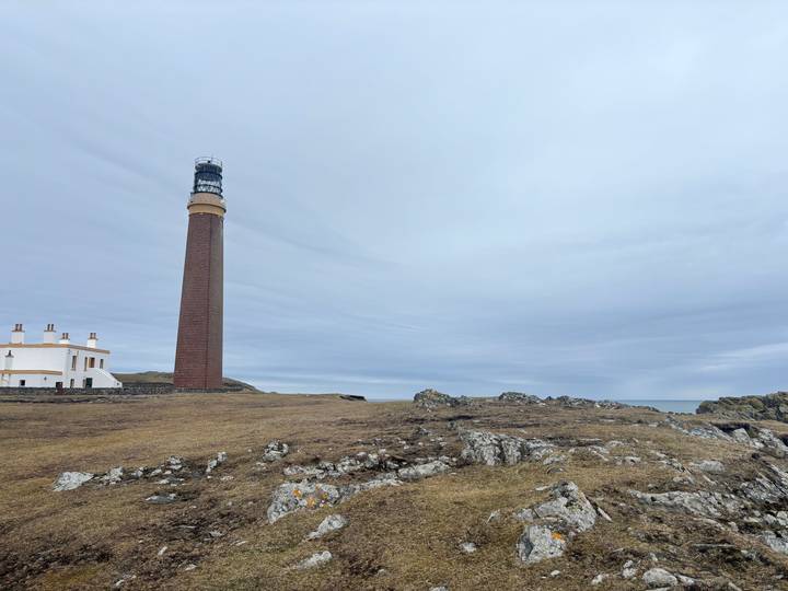 Tall red-brick lighthouse and adjoining white keeper's house on a windswept rocky Scottish coastline