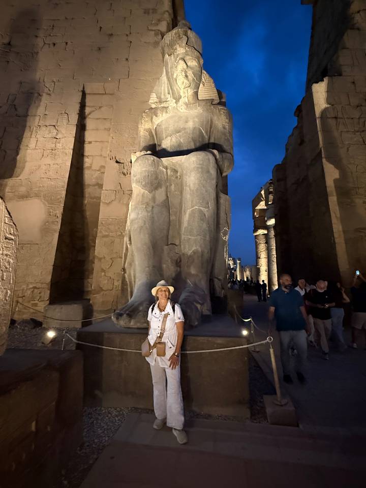 Visitor posing beside colossal ancient statue at Luxor Temple illuminated after dusk.