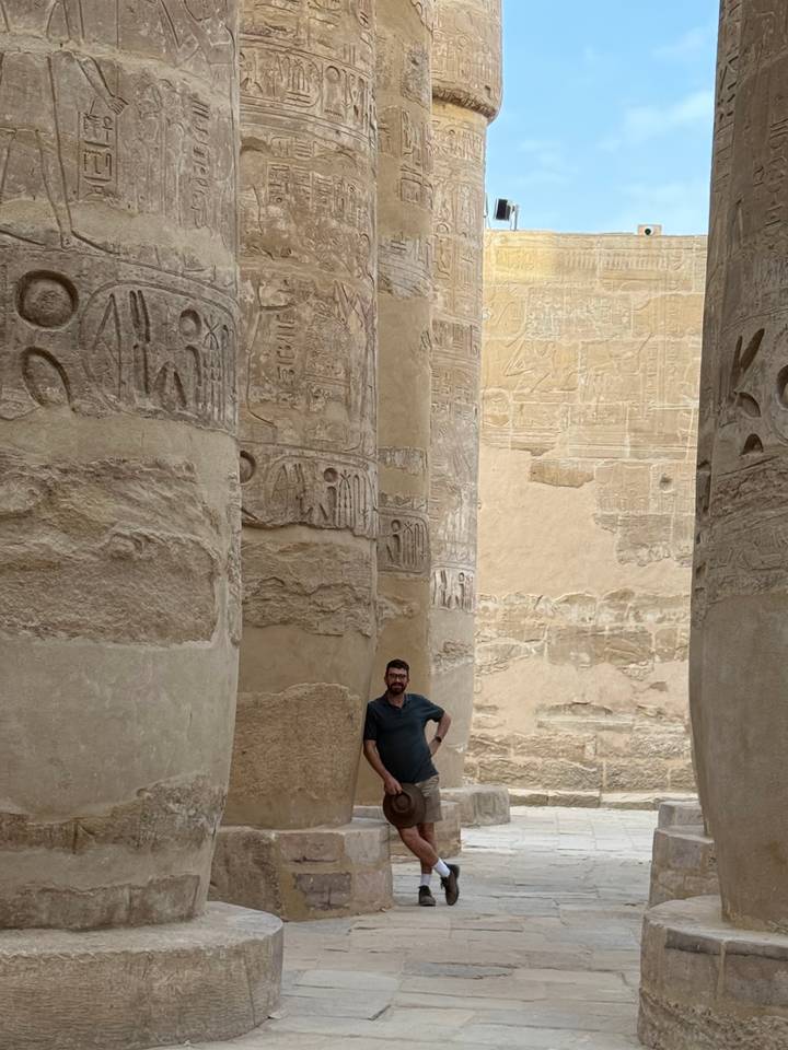 Man posing among giant hieroglyph-covered sandstone columns inside Karnak Temple