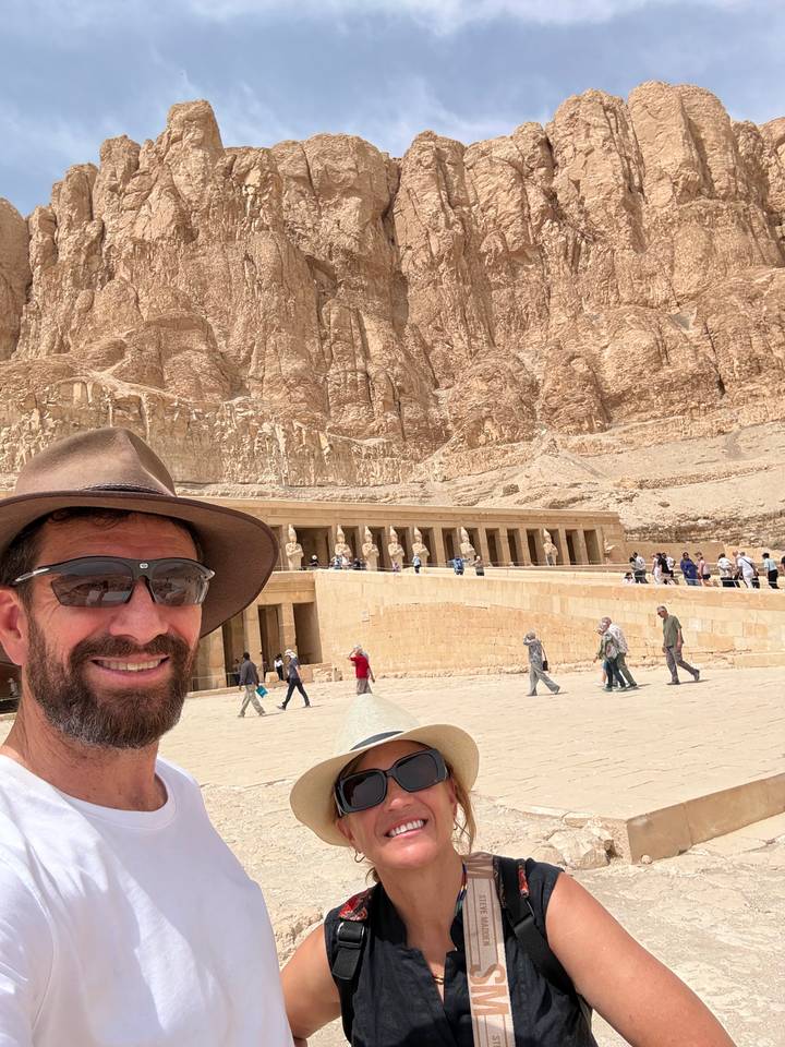 Couple selfie with the terraced Temple of Hatshepsut built into rugged cliffs behind them