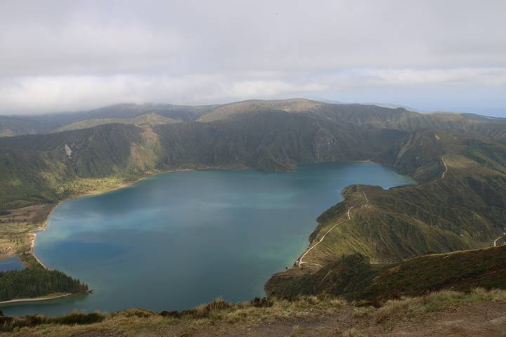 Crater lake with turquoise waters surrounded by steep green volcanic ridges under misty clouds