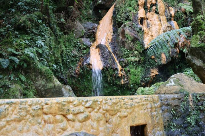 Mineral-rich orange water trickles over mossy rocks in a lush forest thermal spring