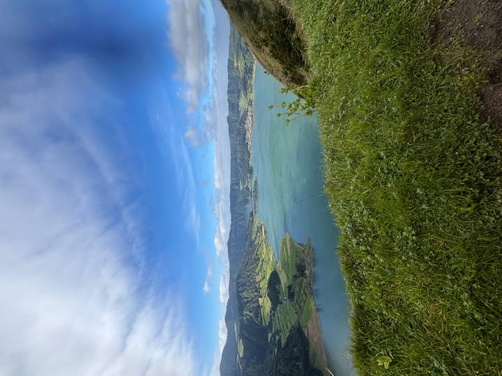 Vivid green crater lake set beneath rolling farmland and dramatic clouds seen from grassy rim