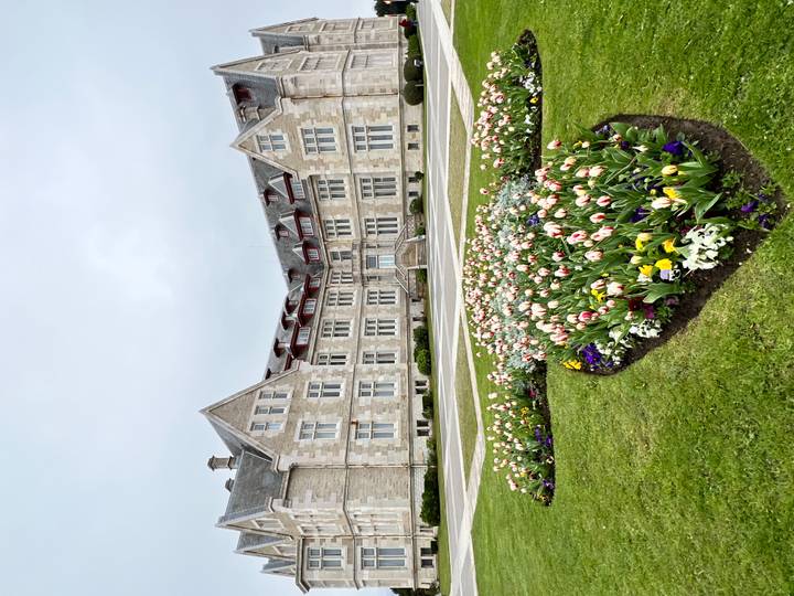 Grand stone palace with gabled roof fronted by manicured lawn and colorful tulip beds.