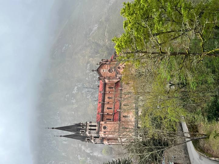 Historic pink stone basilica with twin spires rising against misty mountain backdrop and forested slopes.