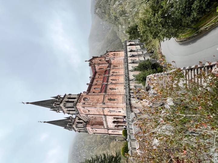 Closer angled view of the Covadonga basilica perched on a hillside road beneath low clouds.