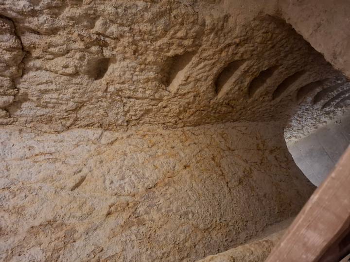 Rough-hewn spiral stairs carved into soft rock descend into an underground chamber.
