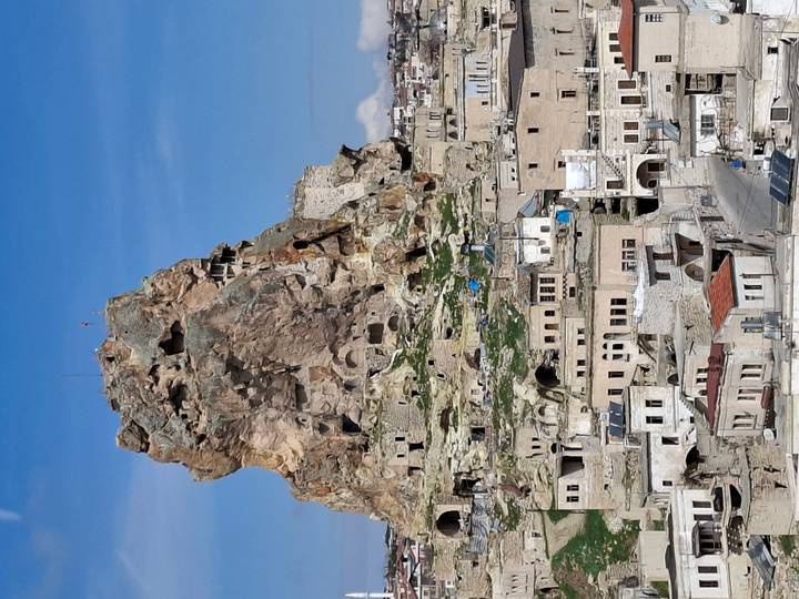 A towering rock citadel rises above a traditional stone town under clear blue skies.