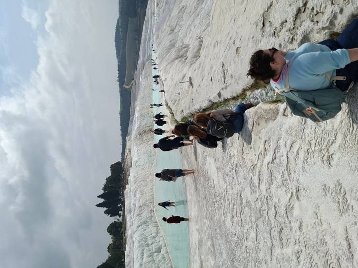 Visitors walk along bright white travertine pools filled with turquoise water.