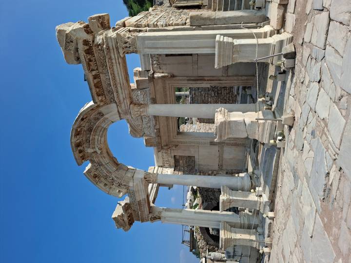 The ornate marble arch and columns of the Temple of Hadrian stand beneath a bright blue sky.