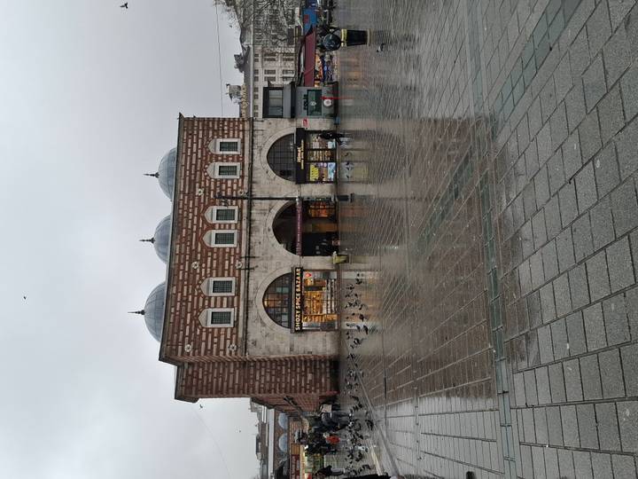 A historic brick bazaar building reflected on a wet plaza during a rainy day.