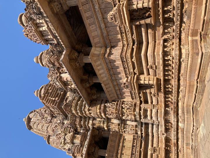 Close-up of intricately carved sandstone temple walls adorned with sculptures under a clear blue sky.