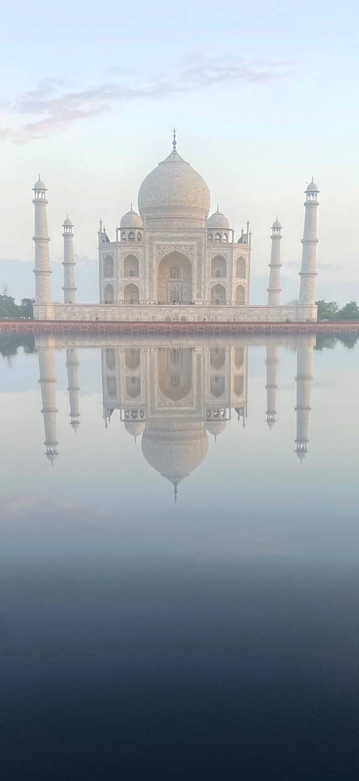A perfectly still reflection of the Taj Mahal appears upside-down in calm water on a misty morning.