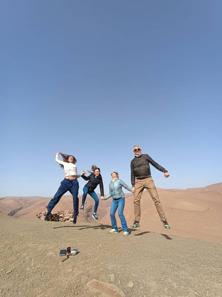 Four friends jump joyfully atop rolling desert hills under a clear blue sky.