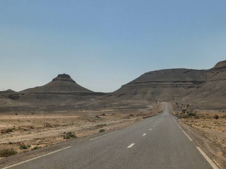 A lonely asphalt road stretches through a barren desert landscape towards distinctive mesas.