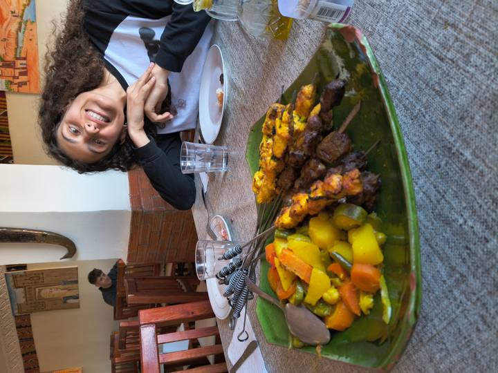 A smiling diner poses behind a plate of skewered meat and vegetables in a casual restaurant.