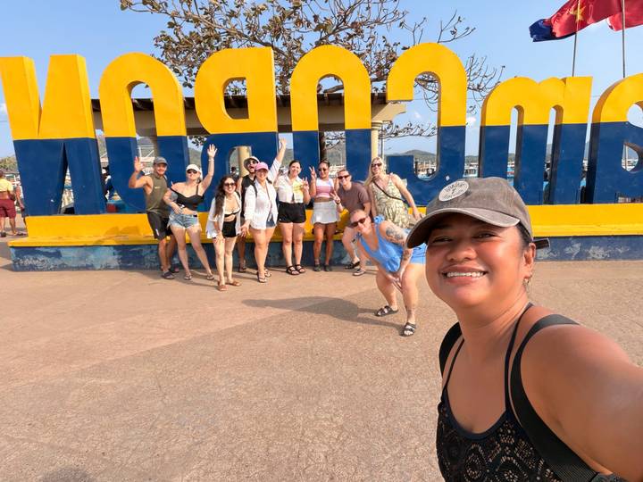 Travelers pose enthusiastically in front of a large colourful Coron town sign.