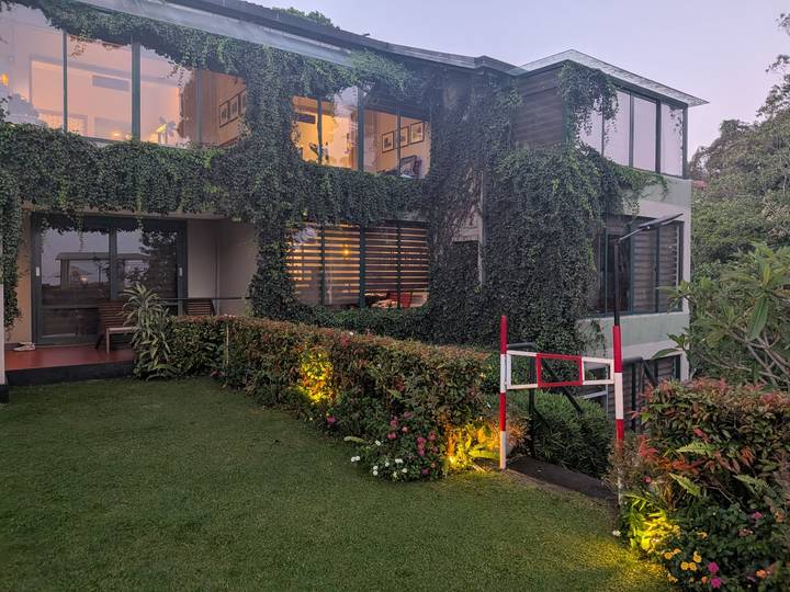 Modern villa covered in cascading vines with a lit garden at dusk.