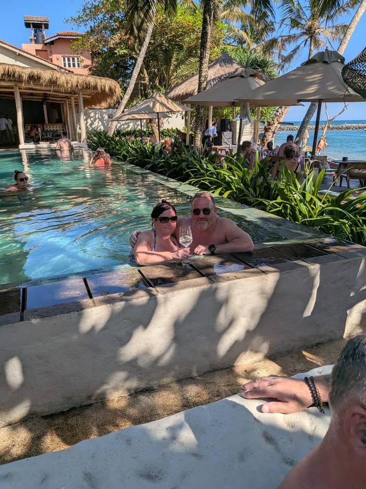 Couple enjoying wine while relaxing in a resort infinity pool with greenery around.