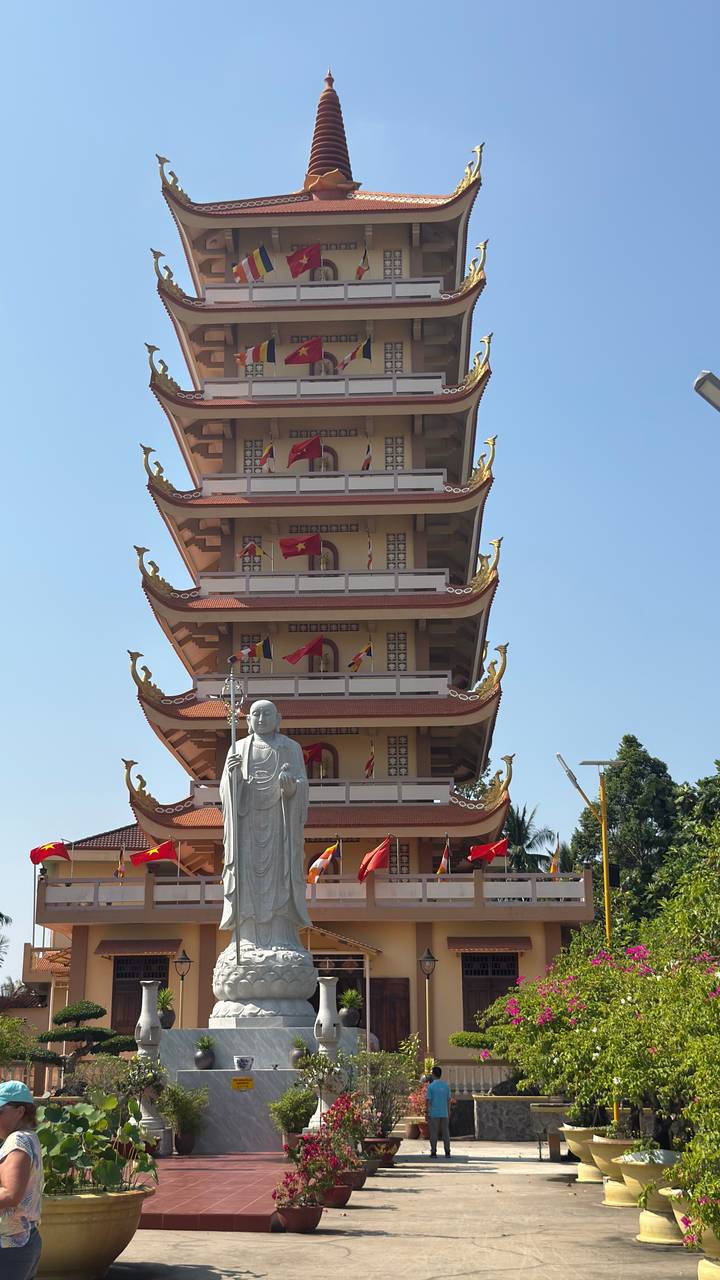 Tall tiered pagoda with a standing Buddha statue in front against clear blue sky