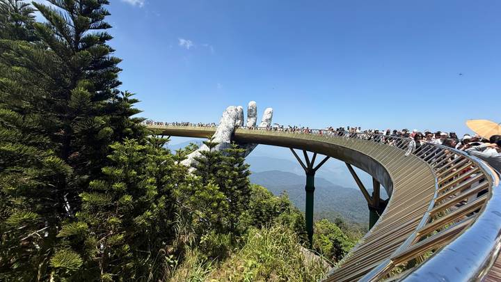 Side view of the curved Golden Bridge crowded with visitors above green forested valley