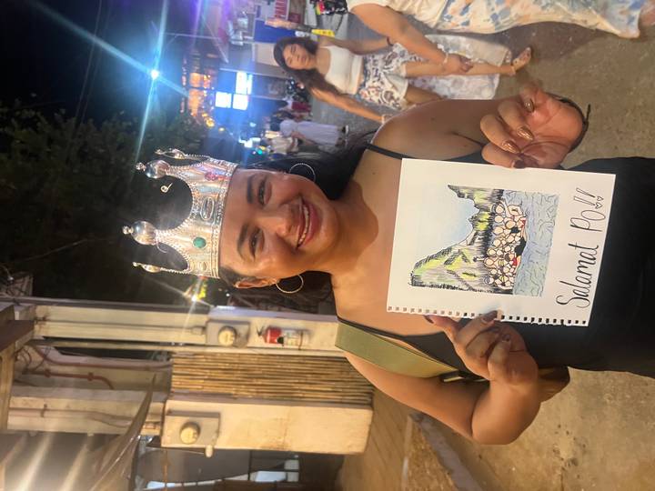 Young woman wearing a playful crown holds a hand-drawn thank-you sign at night market