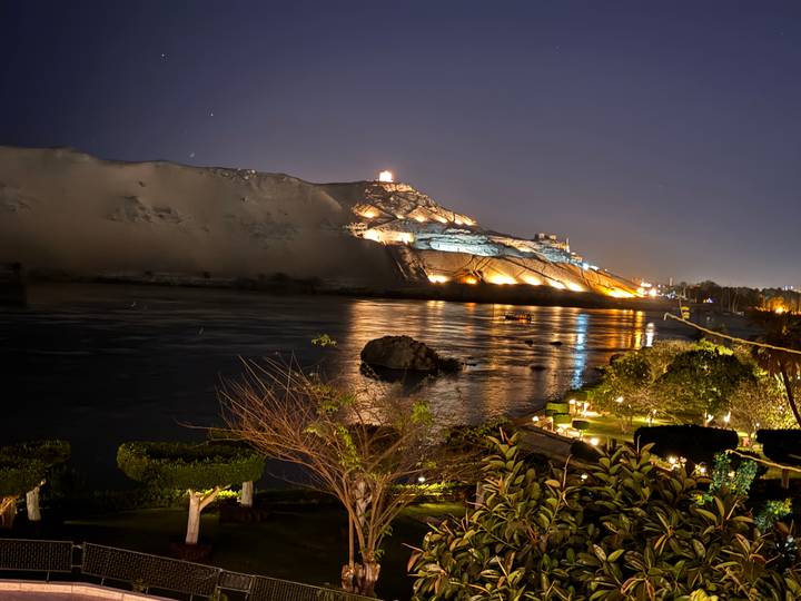 Night view of illuminated mausoleum on desert bluff reflecting across the Nile River