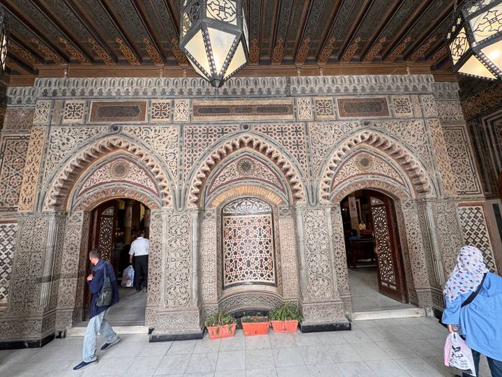 Ornately patterned facade of historic Cairo building with arched doorways and visitors entering