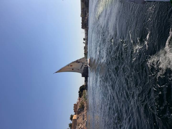 Single felucca with tall lateen sail glides across calm Nile waters