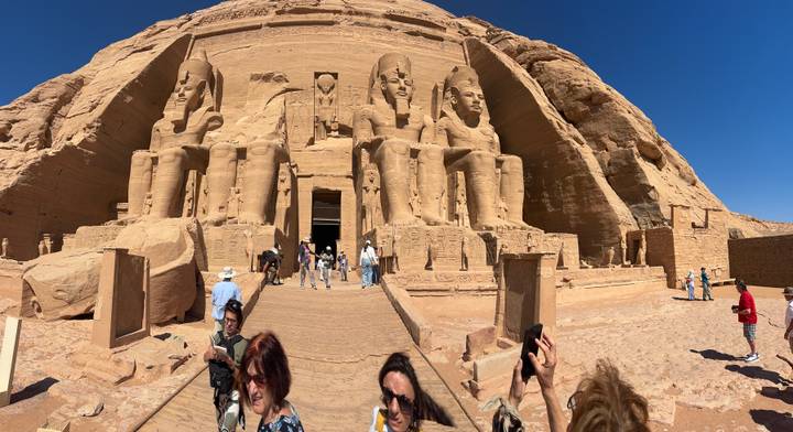Grand façade of Abu Simbel with four colossal seated pharaohs as tourists explore