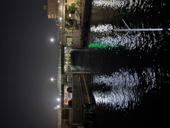 Nighttime view of illuminated lock gate and bridge reflected in dark waters