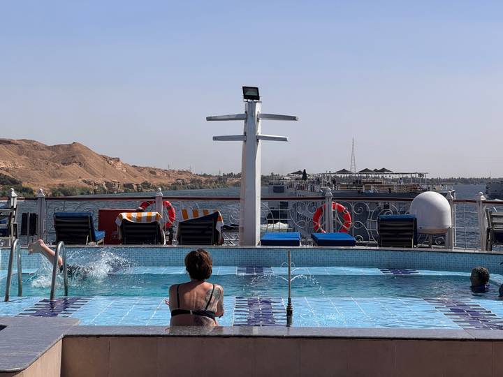 Cruise ship pool deck with guests relaxing while Nile riverbank passes by