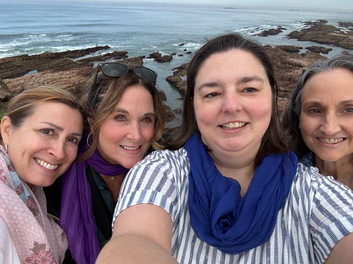 Close-up selfie of four women with rocky Atlantic shoreline and waves behind them.