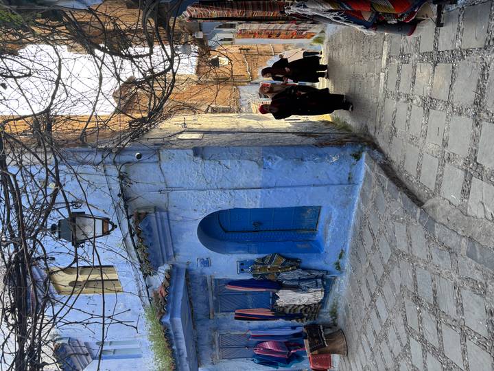 Cobblestone alley of blue-painted buildings in Chefchaouen with three women in traditional dress walking uphill.