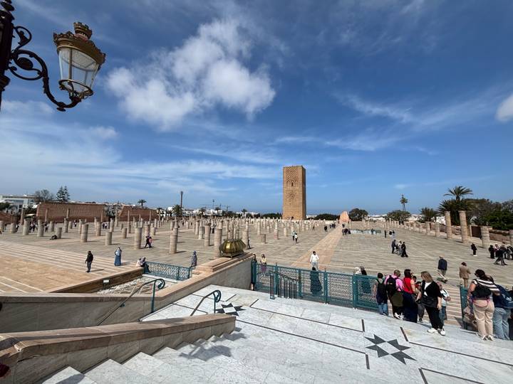 Wide plaza with marble columns and Hassan Tower in Rabat with tourists scattered around under blue skies.