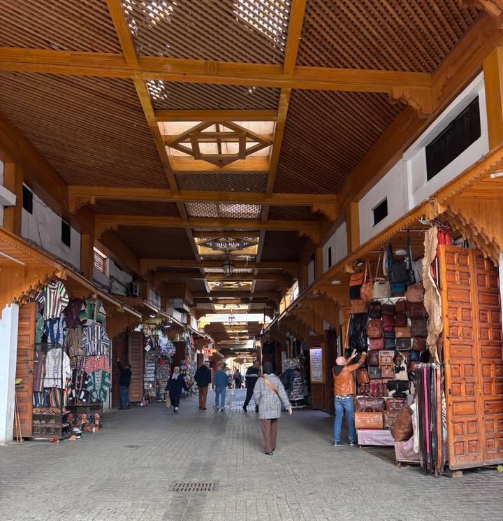 Covered souk lined with leather bags and textiles, wooden ceiling beams and shoppers walking through.