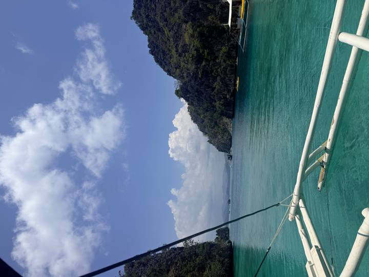 View from a bangka boat of turquoise water and green limestone islands under a partly cloudy sky.