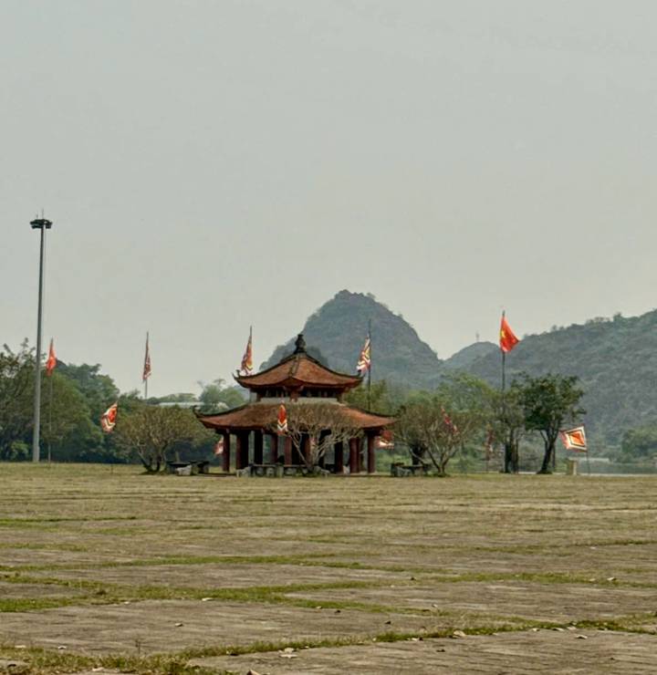 Traditional Vietnamese pavilion with fluttering flags set against karst hills in a large open field