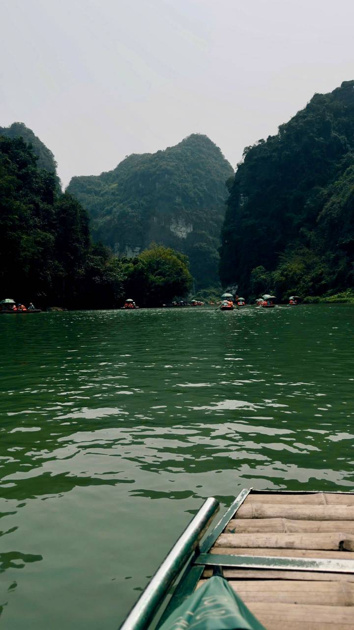 Rowboats with sun umbrellas carrying visitors through a lush limestone gorge on emerald water