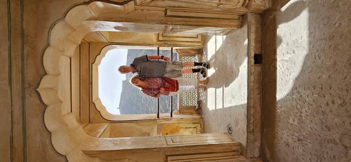 A couple stands in a sun-lit archway of Amber Fort with distant hills visible through the opening.