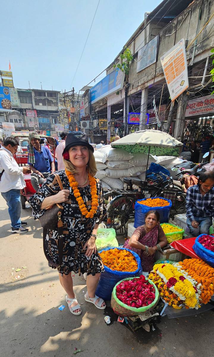 Woman wearing a marigold garland smiles in a bustling Delhi market filled with bright flower baskets and vendors.