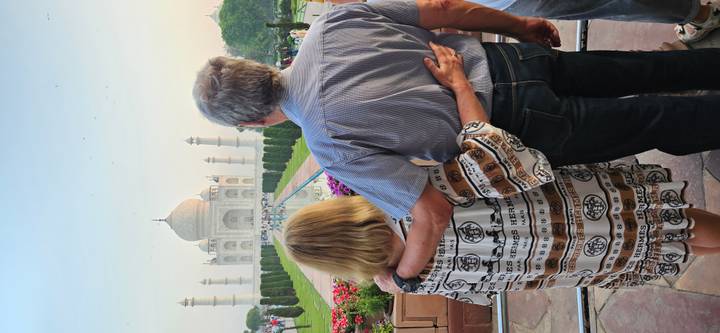 A couple embraces while admiring the early-morning view of the Taj Mahal from the main garden walkway.