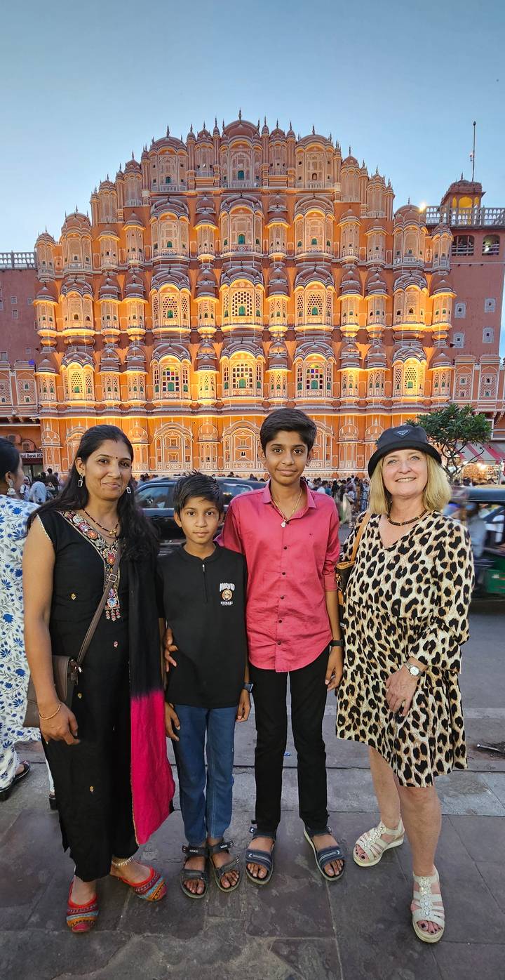 Tourist poses with local family in front of the illuminated Hawa Mahal facade at dusk.