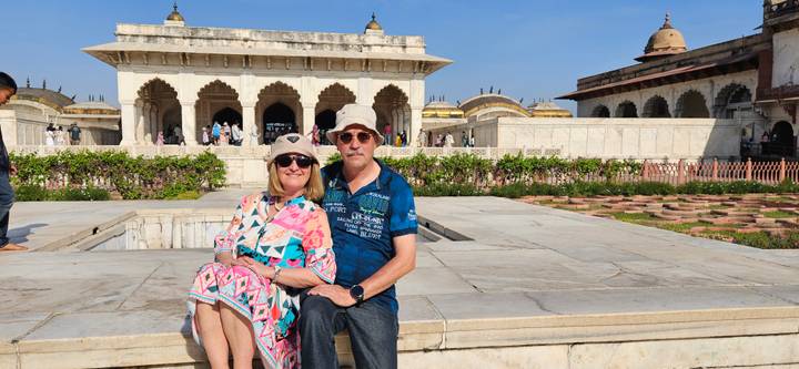 Couple relaxes on a marble ledge inside Agra Fort complex under bright blue skies.